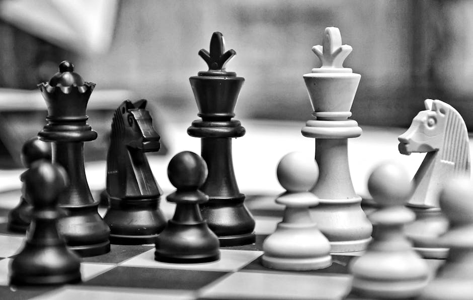 Close-up view of a black-and-white chessboard featuring intricately carved wooden chess pieces, including a king, queen, bishop, knight, and pawns, arranged in mid-game positions. The pieces are placed on a wooden chessboard with alternating dark and light squares, with some pieces in focus and others slightly blurred in the background. The scene appears to be set indoors, with subtle lighting highlighting the textured surfaces of the chess pieces. The image documents the detailed craftsmanship of the chess set, which could be used in an interior or entertainment setting. This type of imagery aligns with themes of strategic thinking and precise handling often involved in home or office relocations, such as carefully packing or transporting valuable items like chess sets during a move, which companies like Man with Van North End may assist with in the context of house removals or packing and moving services.